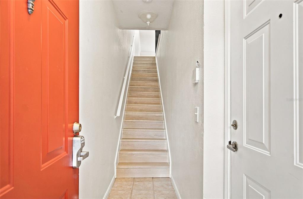 A staircase with light wood steps sits between a bright orange door and a white door — 2151 CHIANTI PLACE UNIT 12-122, PALM HARBOR, FL