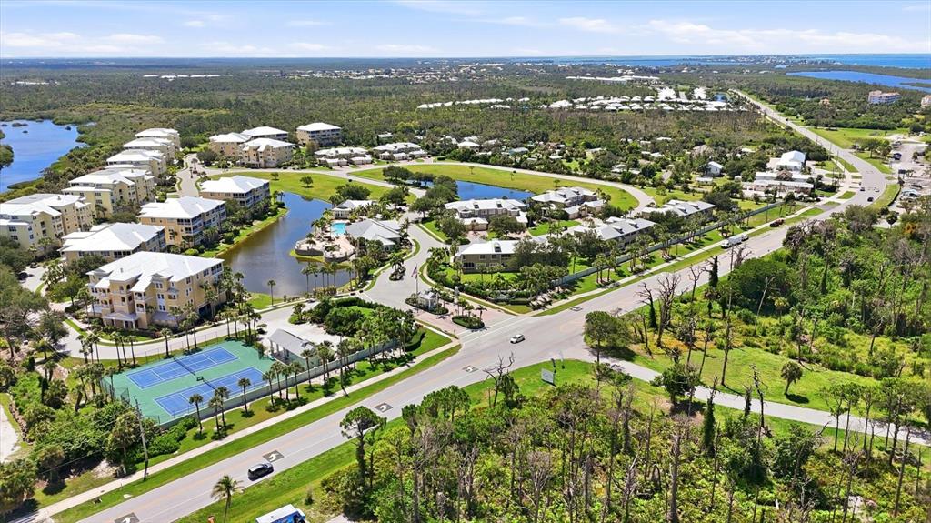An aerial view shows a residential complex with multi-story buildings, a pond, and tennis courts — 10600 LEMON CREEK LOOP UNIT 104, ENGLEWOOD, FL