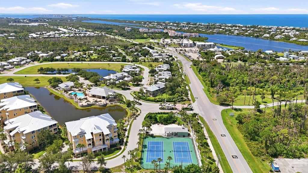 An aerial view shows a residential complex with a pool, tennis courts, and nearby water — 10600 LEMON CREEK LOOP UNIT 104, ENGLEWOOD, FL