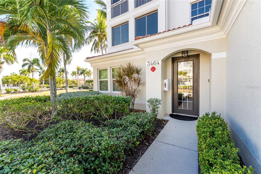 The exterior view shows a building entrance with a glass door, landscaping, and palm trees — 3464 SUNSET KEY CIRCLE UNIT 103, PUNTA GORDA, FL