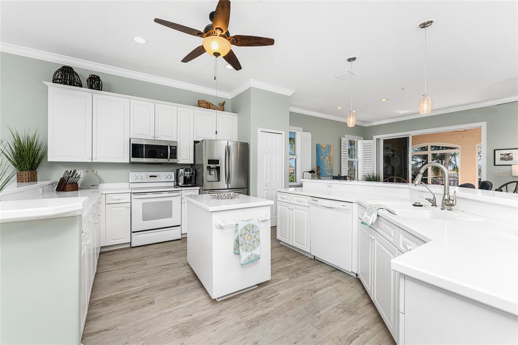 A kitchen features white cabinetry, a central island, stainless steel appliances, and light wood flooring — 3464 SUNSET KEY CIRCLE UNIT 103, PUNTA GORDA, FL