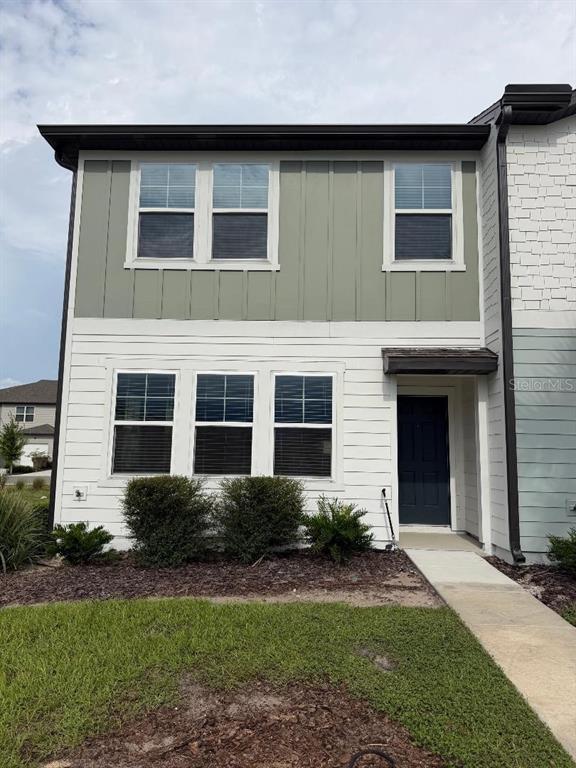 A two-story townhouse exterior features white horizontal siding, green vertical siding, and a dark door — 393 GRAND PINE LANE, ST CLOUD, FL