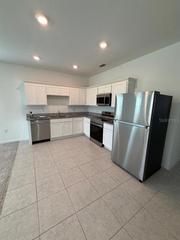 A kitchen features white cabinets, stainless steel appliances, and light-colored tile flooring — 393 GRAND PINE LANE, ST CLOUD, FL