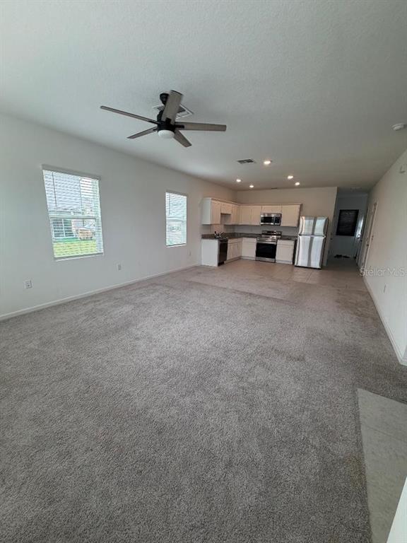 An open-concept living area with carpeted flooring leads to a kitchen with white cabinets — 393 GRAND PINE LANE, ST CLOUD, FL
