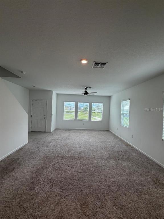An empty living room features beige carpeting, white walls, a ceiling fan, and three windows — 393 GRAND PINE LANE, ST CLOUD, FL