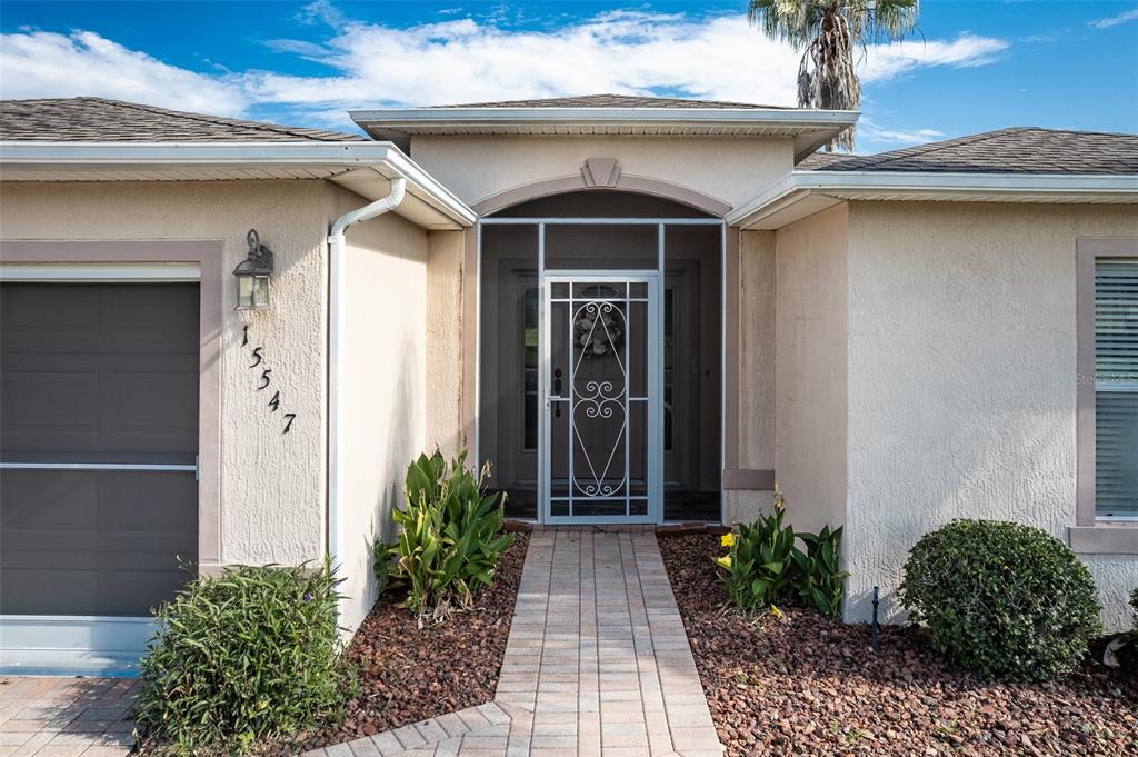 The exterior of a house features a paved walkway leading to a screened front door — 15547 SW 13TH CIRCLE, OCALA, FL