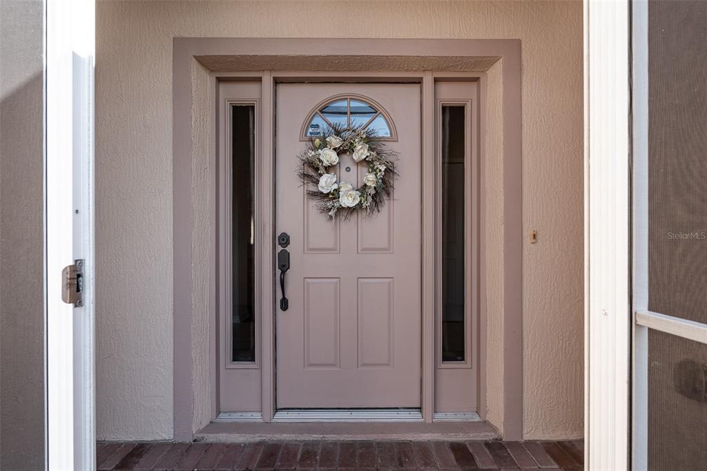 A front door with a floral wreath and sidelights is framed by a beige exterior — 15547 SW 13TH CIRCLE, OCALA, FL