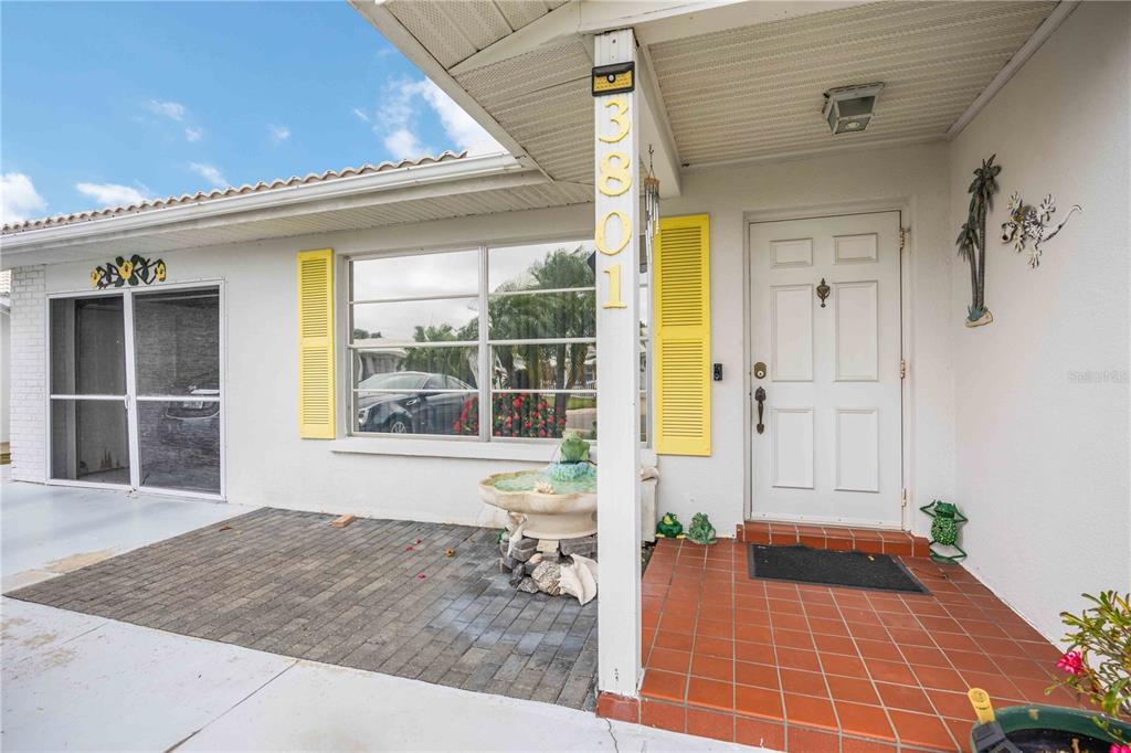 The exterior of a house features a brick patio, a white front door, and yellow shutters — 3801 CHINABERRY, BRADENTON, FL