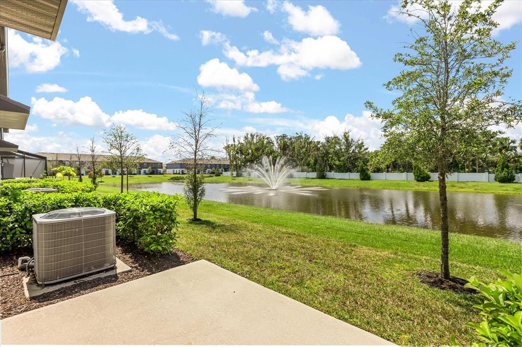A concrete patio overlooks a grassy lawn, a pond with a fountain, and neighboring houses — 366 CAPE HONEYSUCKLE PLACE, SANFORD, FL