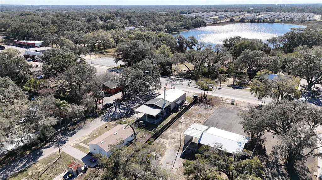 An aerial view shows several buildings, a parking area, and a lake surrounded by trees — 10 BARRY AVENUE, MASCOTTE, FL