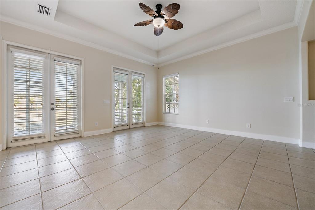A spacious room with beige tile flooring, a tray ceiling, and two sets of French doors — 423 MANNS HARBOR DRIVE, APOLLO BEACH, FL