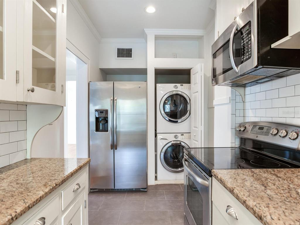 A kitchen with white cabinets, granite countertops, stainless steel appliances, and a stacked laundry unit — 2114 W DEKLE AVENUE UNIT 4, TAMPA, FL