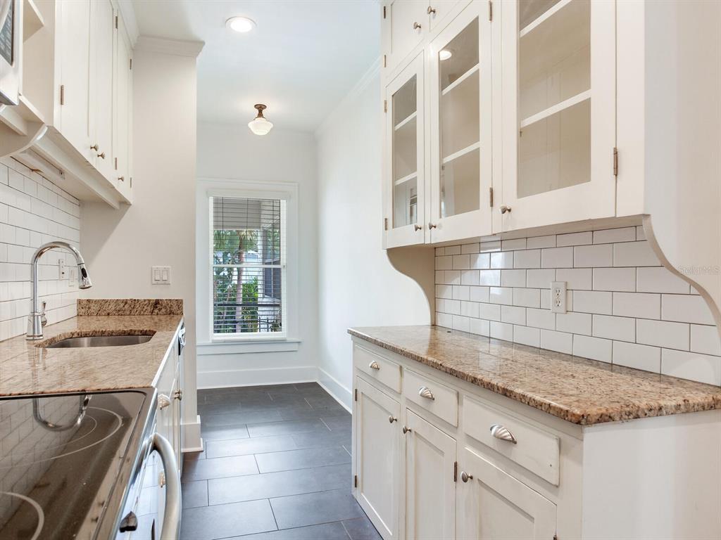 A galley kitchen features white cabinets, granite countertops, subway tile backsplashes, and dark tile flooring — 2114 W DEKLE AVENUE UNIT 4, TAMPA, FL