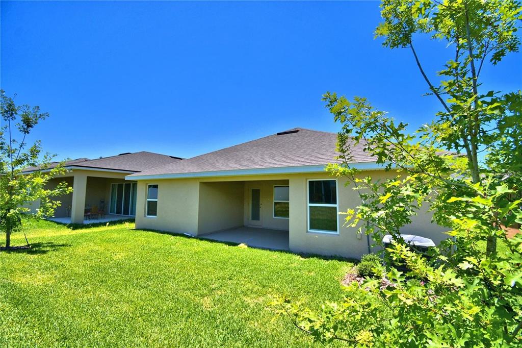 The rear exterior of a tan stucco house features a covered patio and grassy yard — 3640 LINDBERGH STREET, LAKELAND, FL