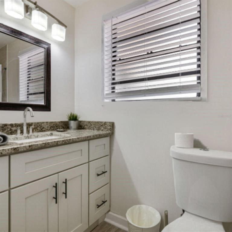 A bathroom features a granite vanity, a white cabinet, a mirror, and a window with blinds — 1202 PRINCETON RD, COCOA, FL