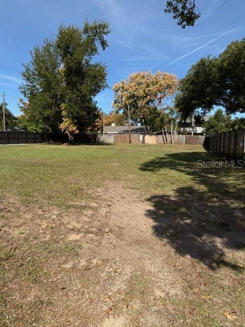 A large, grassy vacant lot is enclosed by a dark wooden fence under a blue sky — EAST, CLERMONT, FL