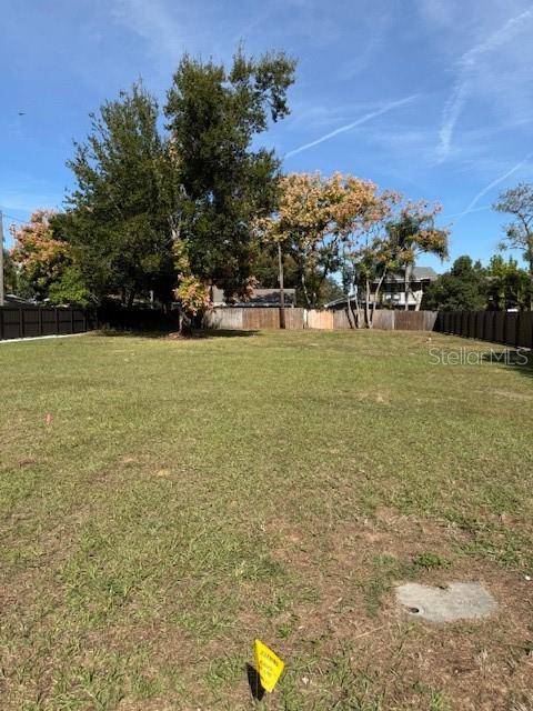A vacant, grassy residential lot is enclosed by wooden fencing and surrounded by mature trees — EAST, CLERMONT, FL