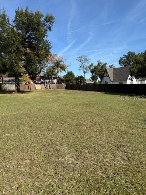 A grassy, vacant residential lot is enclosed by a dark wooden fence under a blue sky — EAST, CLERMONT, FL
