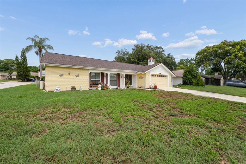 A yellow, single-story ranch-style house with a driveway and a large front lawn — 12301 HOUNDS BAY ROW, HUDSON, FL
