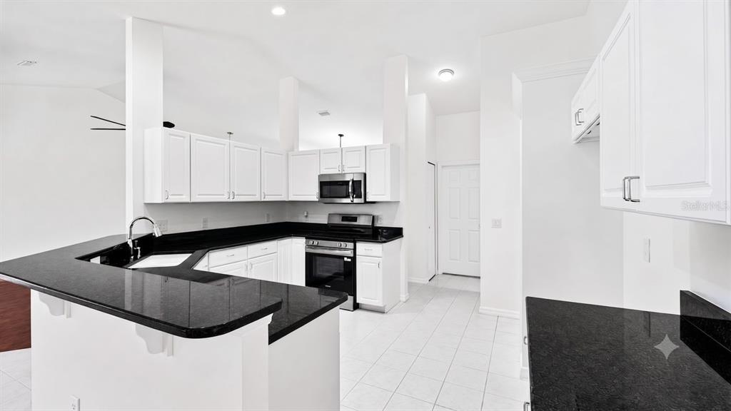 A kitchen features white cabinets, black countertops, stainless steel appliances, and white tile flooring — 3325 INDIAN TRAIL, EUSTIS, FL