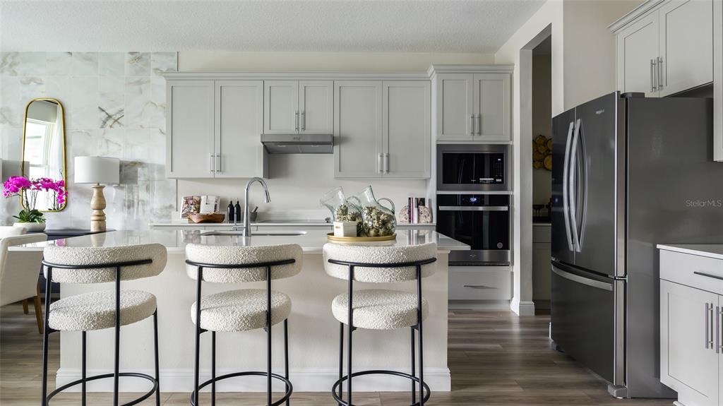 A modern kitchen features light gray cabinets, stainless steel appliances, and a white island with stools — 33607 TWILIGHT SEA PLACE, DADE CITY, FL