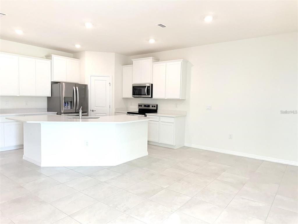 A modern kitchen features white cabinets, stainless steel appliances, a large island, and tile flooring — 4730 NW 39TH STREET ROAD, OCALA, FL