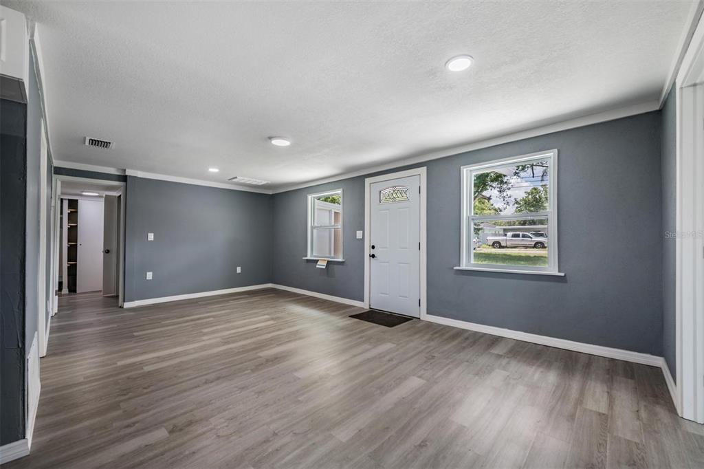 An empty living room features gray walls, light wood-look flooring, recessed lighting, and a front door — 636 STREMMA ROAD, LARGO, FL