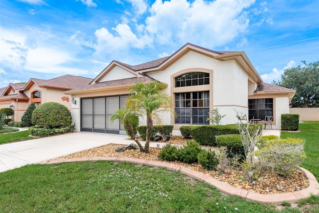 A single-story house with a beige stucco exterior, a screened garage, and a landscaped front yard — 13825 LEROUX DRIVE, HUDSON, FL
