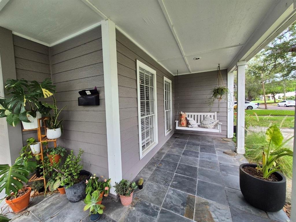 A covered front porch features gray siding, slate tile flooring, a hanging swing, and potted plants — 2910 W SITIOS STREET, TAMPA, FL