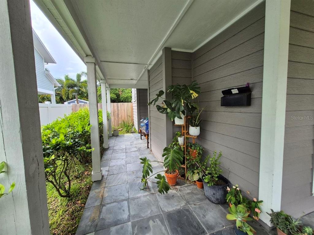 A covered outdoor patio features gray tiled flooring, horizontal siding, and several potted plants — 2910 W SITIOS STREET, TAMPA, FL