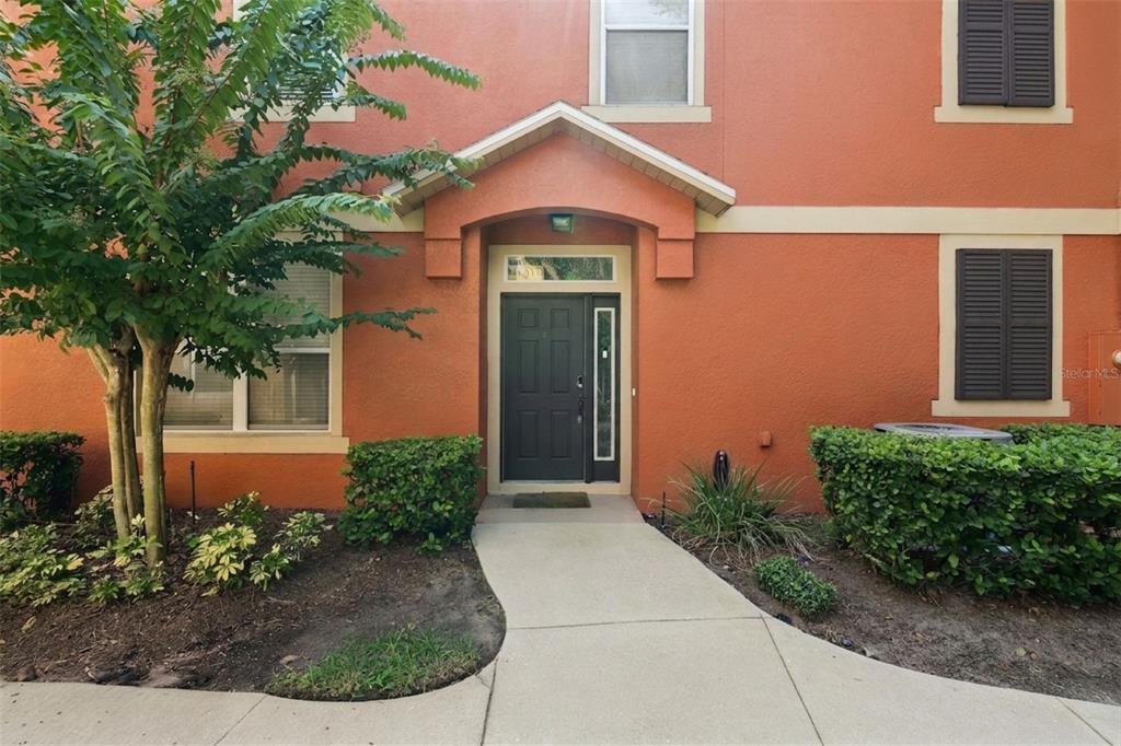 A concrete walkway leads to the dark front door of an orange two-story building — 1610 PINE OAK TRAIL, SANFORD, FL