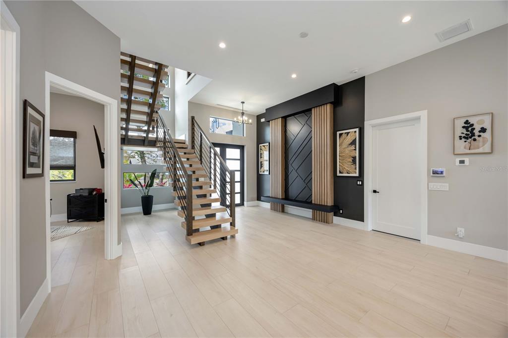 A modern foyer features light wood flooring, a floating staircase, and a geometric accent wall — 2314 PROSPECT STREET, SARASOTA, FL