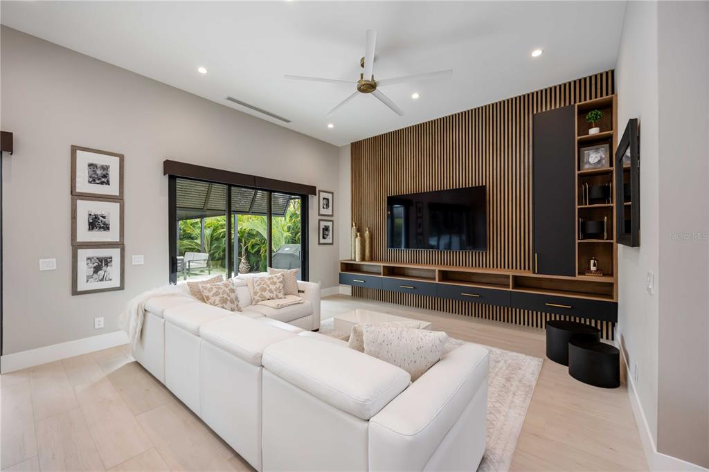 A modern living room features a white sectional sofa, wood-slatted accent wall, and sliding glass doors — 2314 PROSPECT STREET, SARASOTA, FL