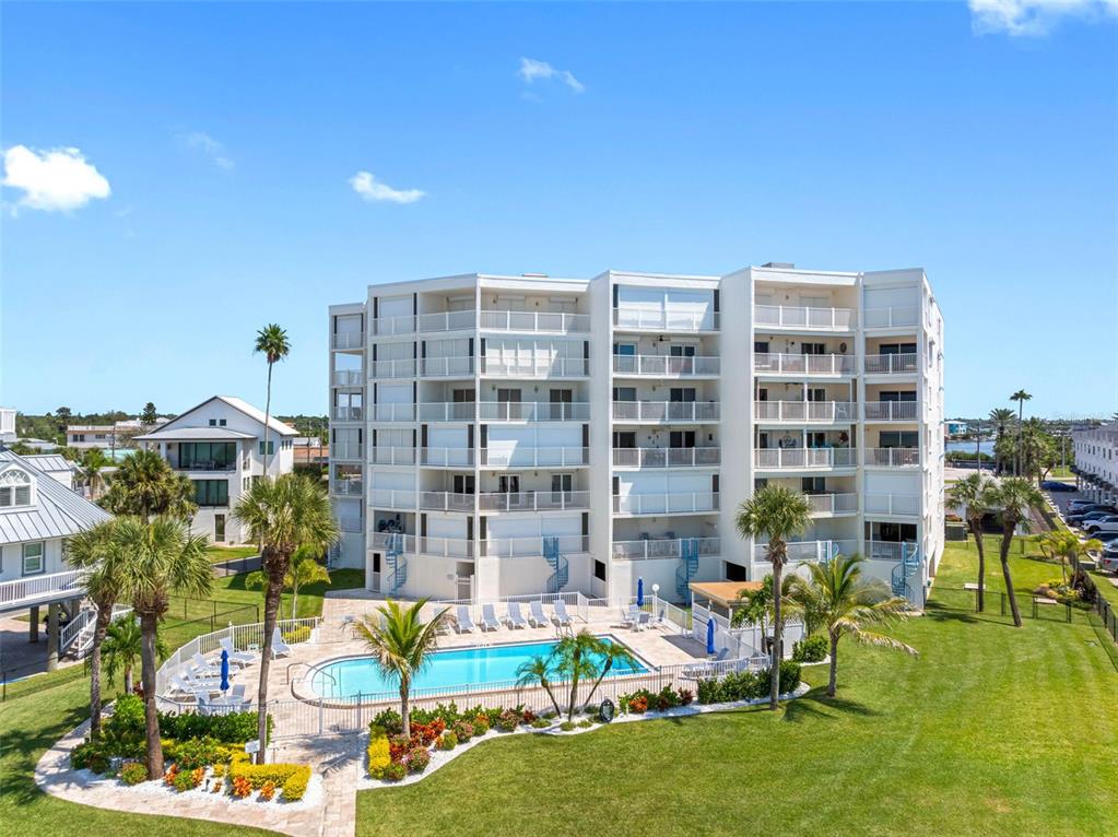 An exterior view of a multi-story apartment building with a swimming pool and palm trees — 17980 GULF BOULEVARD UNIT 401, REDINGTON SHORES, FL