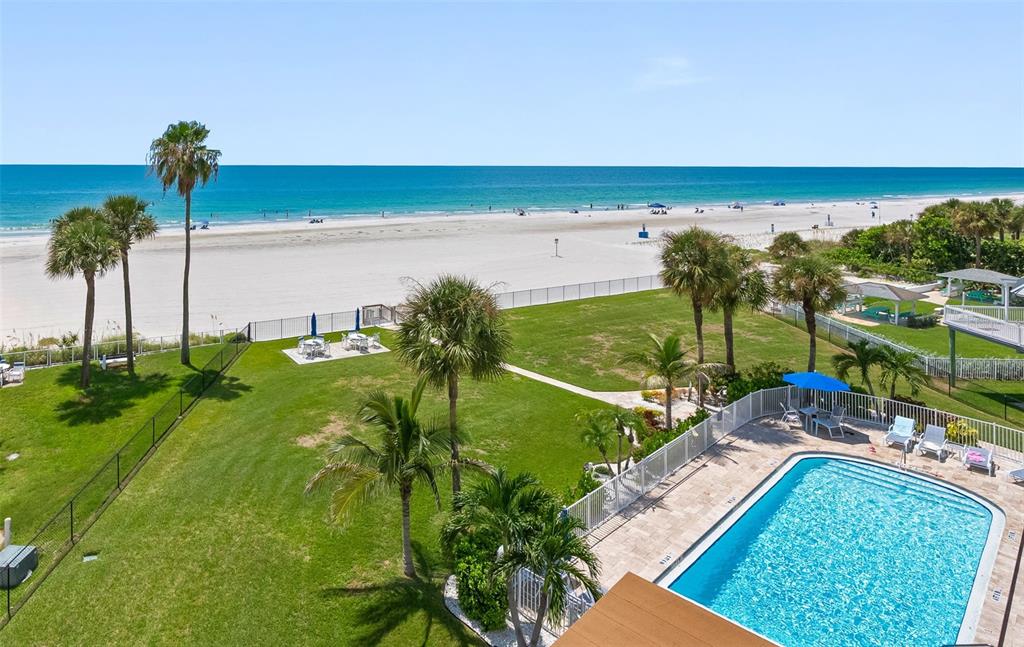 An elevated view of a swimming pool, grassy lawn, and palm trees overlooking a sandy beach — 17980 GULF BOULEVARD UNIT 401, REDINGTON SHORES, FL