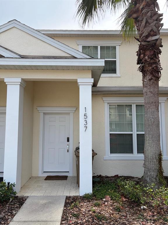 A beige two-story townhouse exterior features a white front door, a columned porch, and palm tree — 1537 TRANQUIL AVENUE, CLERMONT, FL