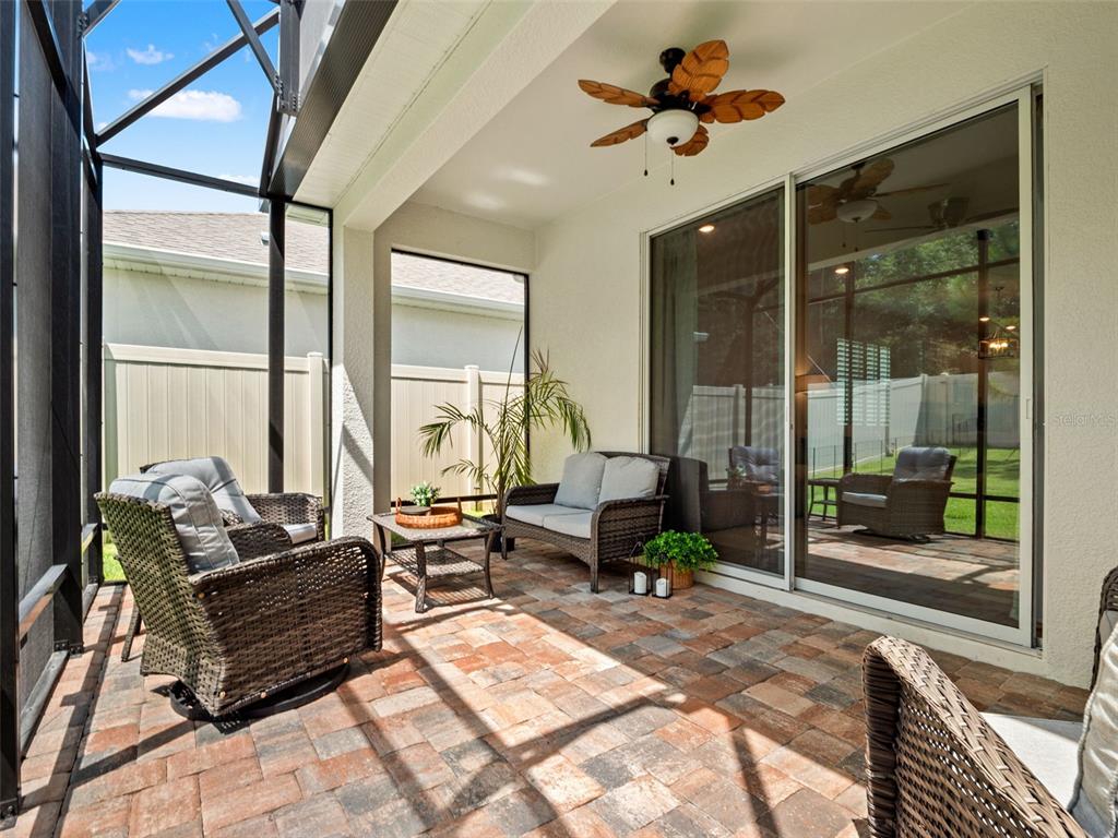 A covered patio features wicker furniture, a ceiling fan, and brick pavers enclosed by screens — 2325 SIRENA LANE, MOUNT DORA, FL