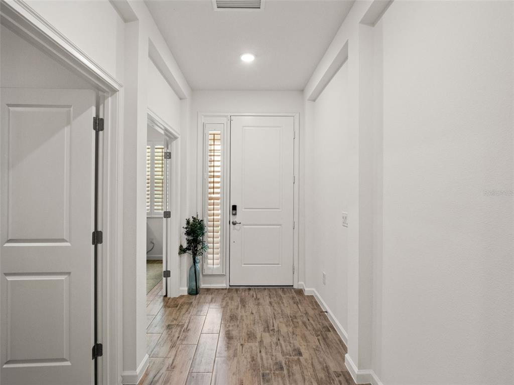 A bright entryway features a white front door, light wood-look tile flooring, and white walls — 2325 SIRENA LANE, MOUNT DORA, FL