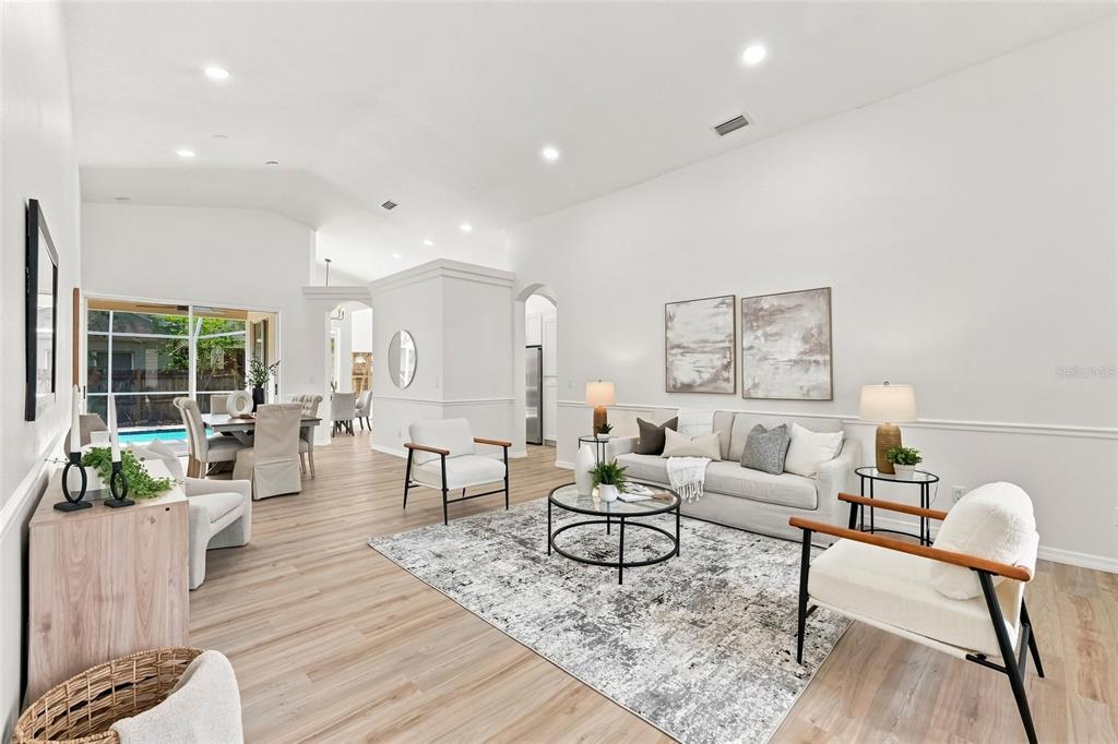 A bright, open-concept living room features light wood flooring, a neutral sofa, and a pool view — 1887 WOOD BEND STREET, TARPON SPRINGS, FL