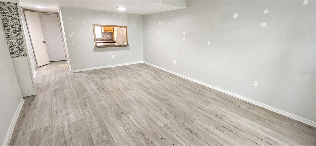 An empty room features light gray wood-look flooring, light gray walls with patch marks, and a pass-through window — 2405 SE 16TH AVENUE UNIT B, OCALA, FL