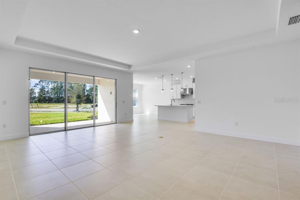A modern kitchen features white cabinetry, a central island, stainless steel appliances, and marble-patterned backsplash — 672 JUNONIA BOULEVARD, NEW SMYRNA BEACH, FL