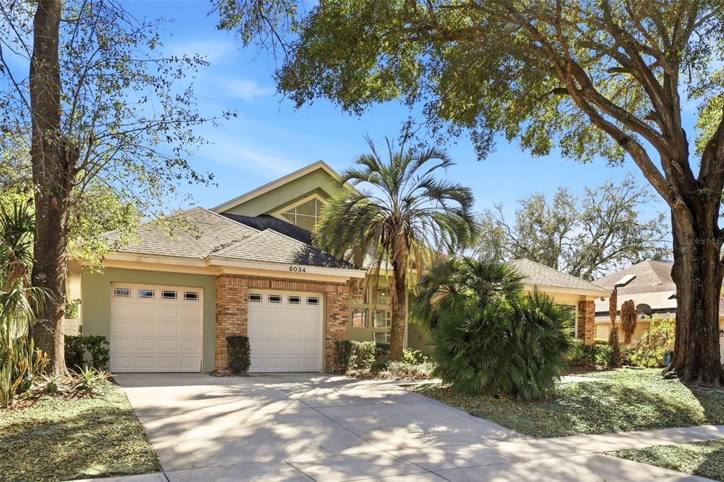A two-story house with a two-car garage, brick accents, and mature trees in the yard — 8034 LANDGROVE COURT, ORLANDO, FL