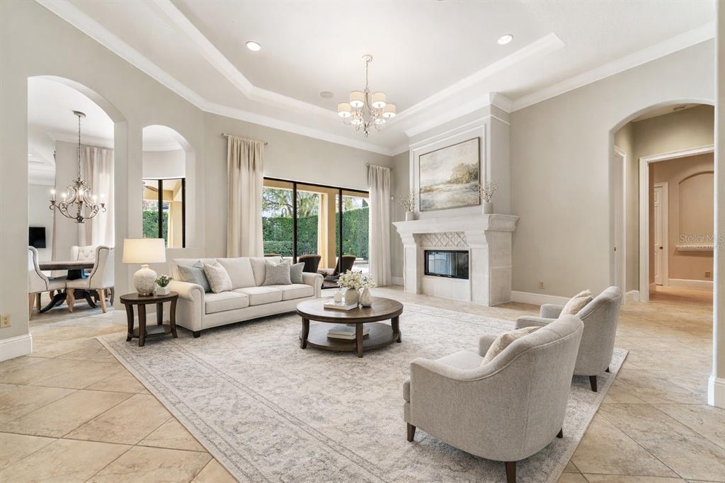 A spacious living room features a stone fireplace, neutral furniture, and a tray ceiling — 6560 LAKE BURDEN VIEW DRIVE, WINDERMERE, FL