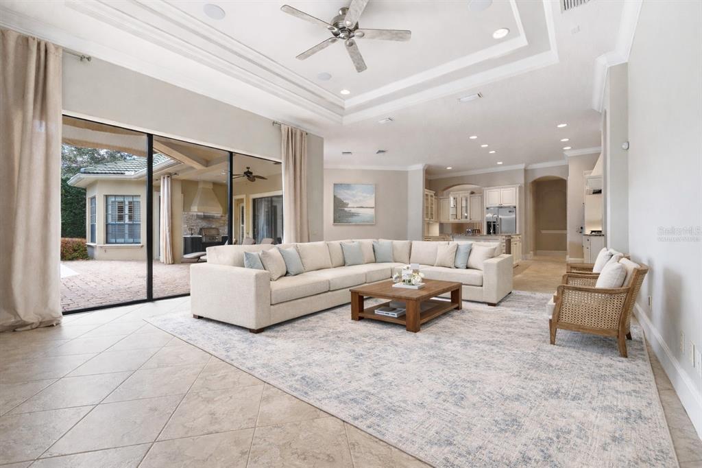 A spacious living room with a large sectional sofa, tray ceiling, and sliding glass doors — 6560 LAKE BURDEN VIEW DRIVE, WINDERMERE, FL