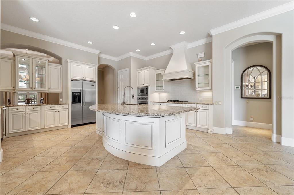 A kitchen with white cabinets, granite countertops, a curved island, and light-colored tile flooring — 6560 LAKE BURDEN VIEW DRIVE, WINDERMERE, FL