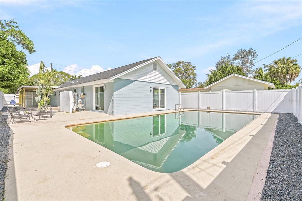 A backyard features a swimming pool, a light blue house, and a white privacy fence — 1811 49TH STREET N, ST PETERSBURG, FL