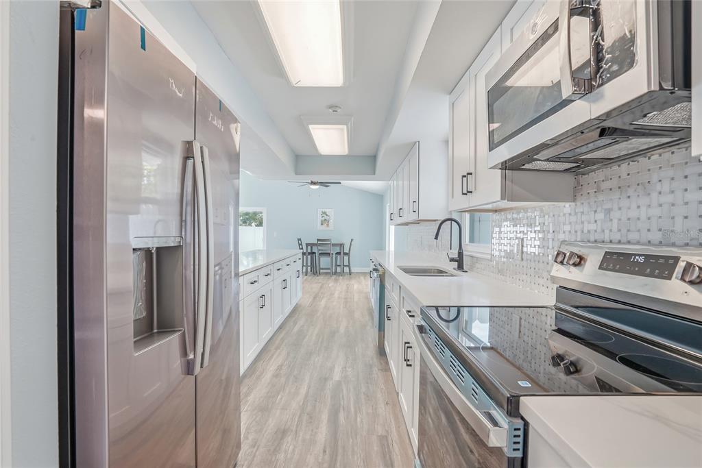 A modern kitchen features white cabinets, stainless steel appliances, and light wood-look flooring — 1811 49TH STREET N, ST PETERSBURG, FL