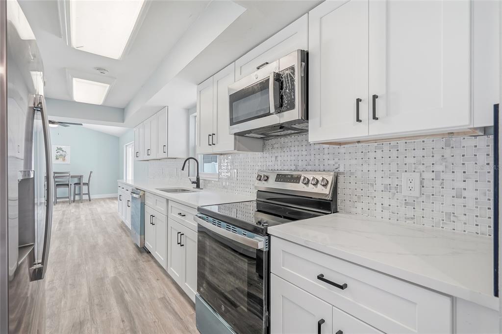 A modern kitchen features white cabinets, stainless steel appliances, marble-look countertops, and a mosaic backsplash — 1811 49TH STREET N, ST PETERSBURG, FL