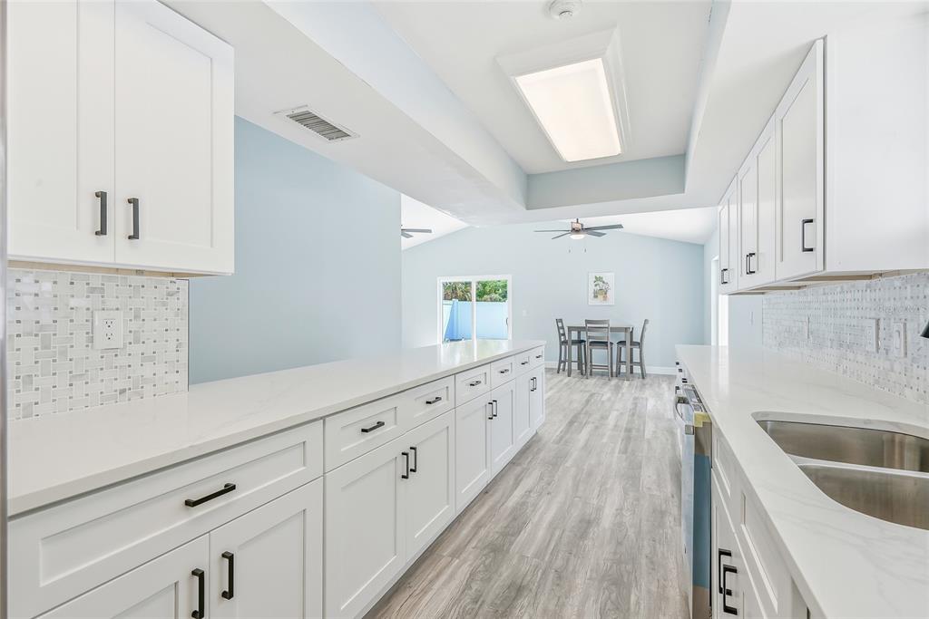 A kitchen with white cabinets, quartz countertops, and light wood-look flooring opens to a dining area — 1811 49TH STREET N, ST PETERSBURG, FL