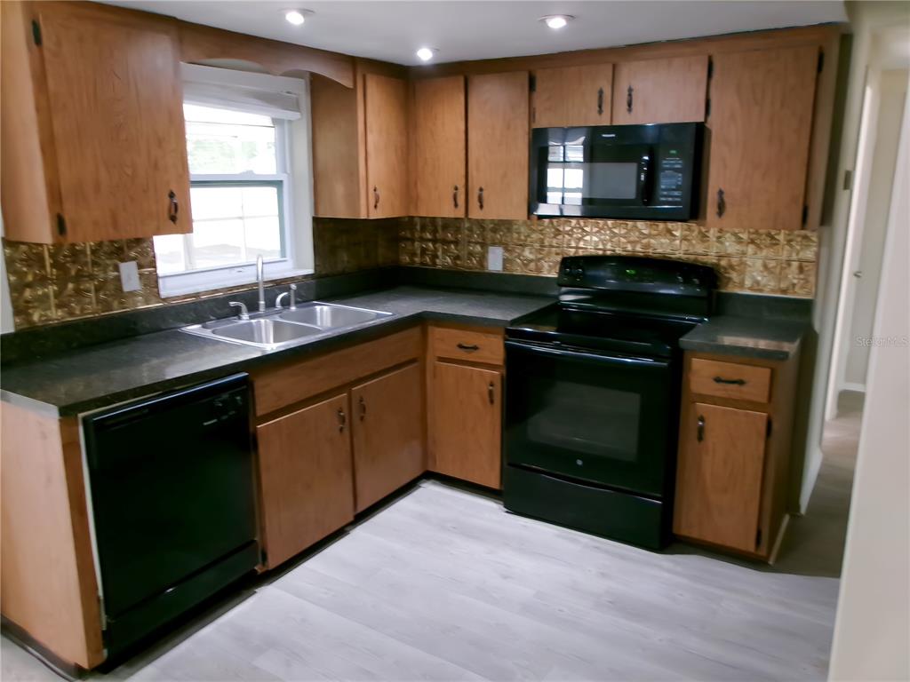 A kitchen features wood cabinets, black appliances, a double sink, and a metallic backsplash — 1421 NORMANDY BOULEVARD, HOLIDAY, FL